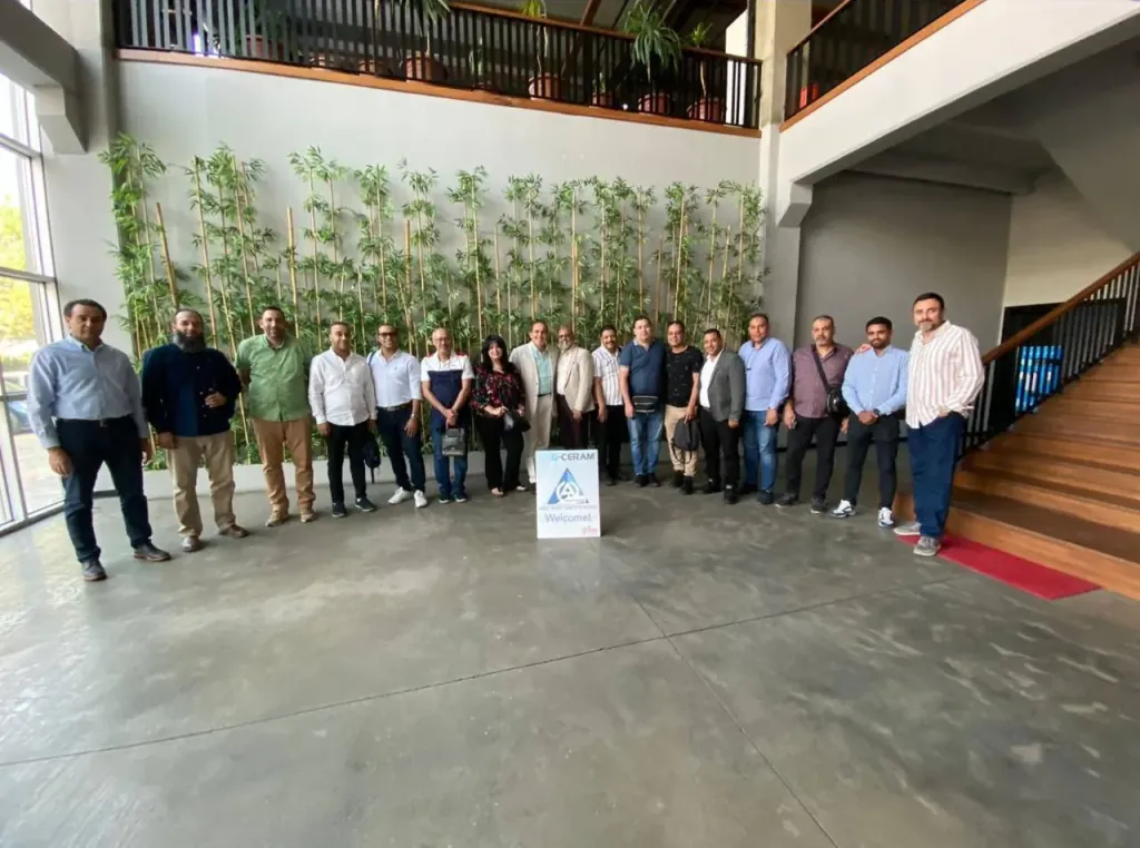 The visiting group standing in a row in a lobby, behind a G-Ceram “Welcome!” sign with the A & O logo