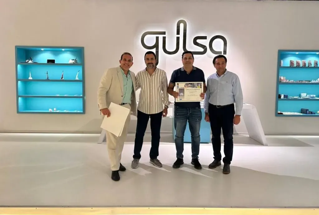 Four men in front of the Gulsa sign, one of them holding a certificate of attendance